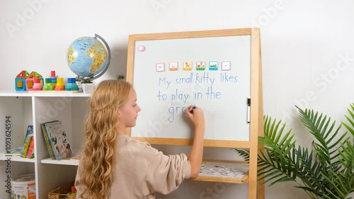 A young girl, a child is having fun learning to build sentences using magnetic word tiles and frames on a whiteboard in a classroom.