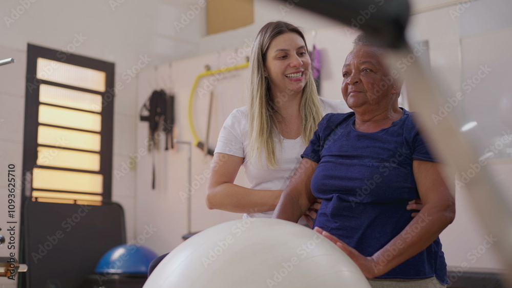Pilates Instructor Assisting Elderly African American Woman in Ball Exercise at Physiotherapy Studio Pilates Instructor Assisting Elderly African American Woman in Ball Exercise at Physiotherapy Studio