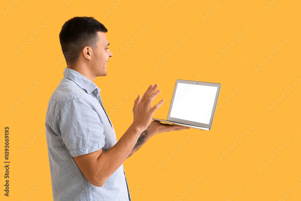 Young man with blank laptop video chatting on yellow background. Online dating concept Young man with blank laptop video chatting on yellow background. Online dating concept