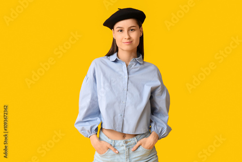 Beautiful young woman in stylish black beret hat on yellow background