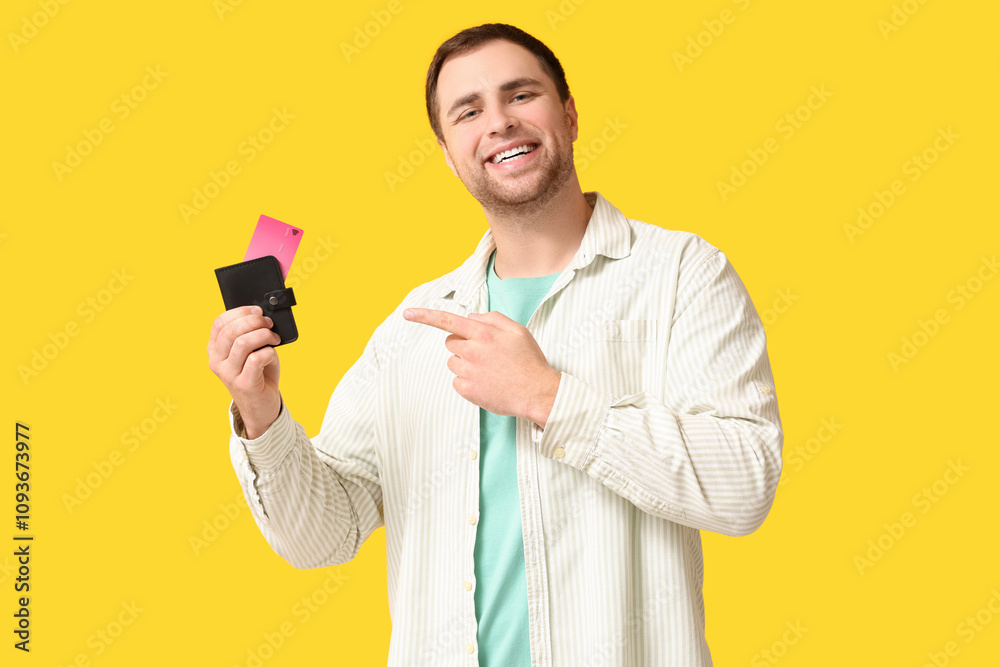 Young man pointing at wallet with credit cards on yellow background Young man pointing at wallet with credit cards on yellow background