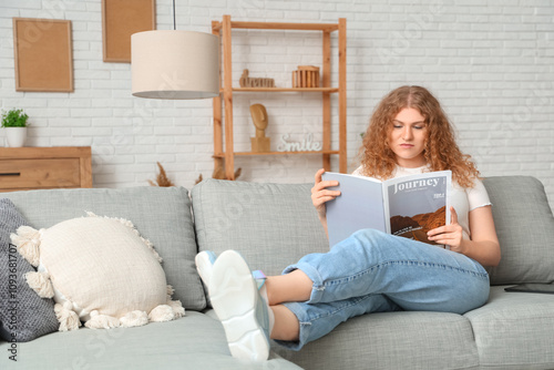 Young woman reading magazine on sofa at home