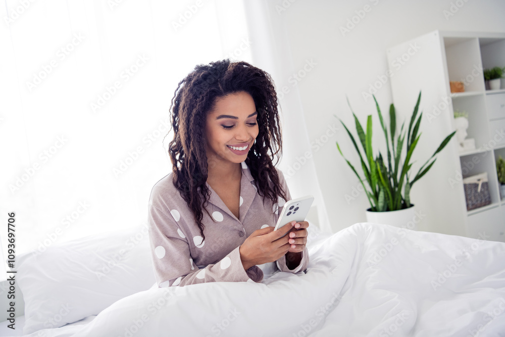Young woman relaxing in bed with phone, embracing natural light and morning comfort Young woman relaxing in bed with phone, embracing natural light and morning comfort
