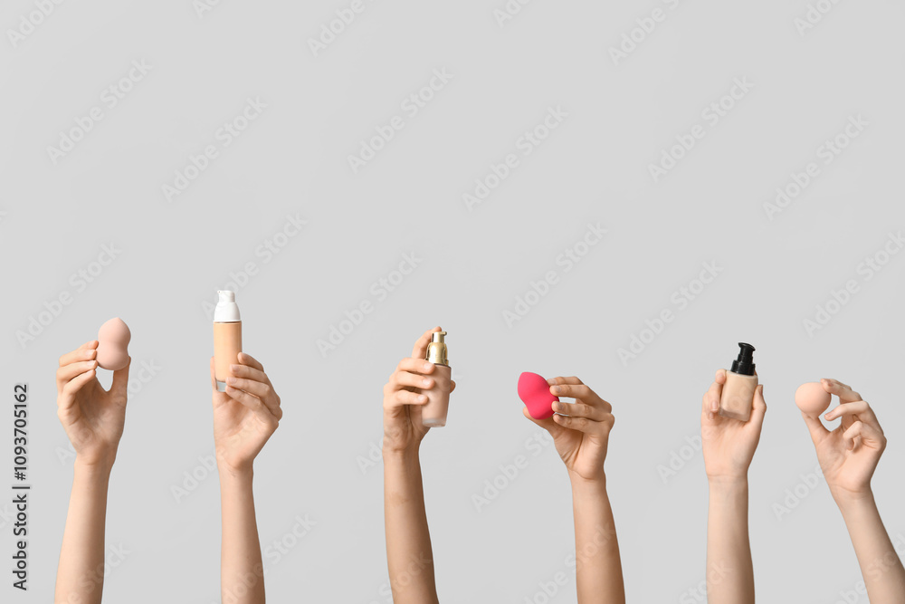 Female hands with bottles of makeup foundation and sponges on grey background Female hands with bottles of makeup foundation and sponges on grey background