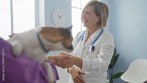 Tableau sur toile A middle-aged blonde woman vet smiles while shaking hands with an adult owner at a veterinary clinic as they discuss care for their pet dog
