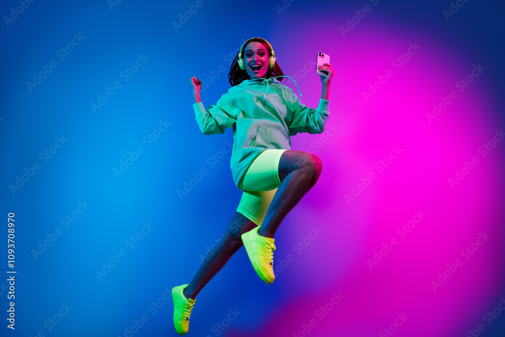 Full length photo of shiny lucky lady dressed green sweatshirt earphones winning game modern gadget isolated blue light color background
