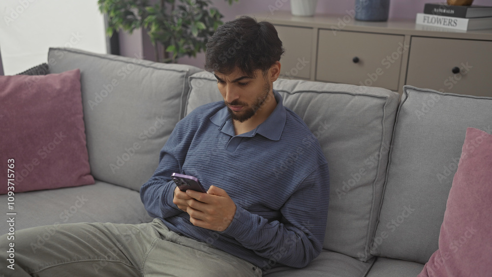 Handsome man using smartphone on cozy sofa in modern apartment interior