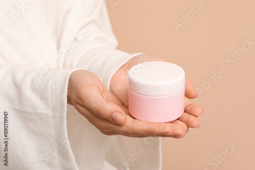 Young woman with jar of cosmetic cream on brown background photo