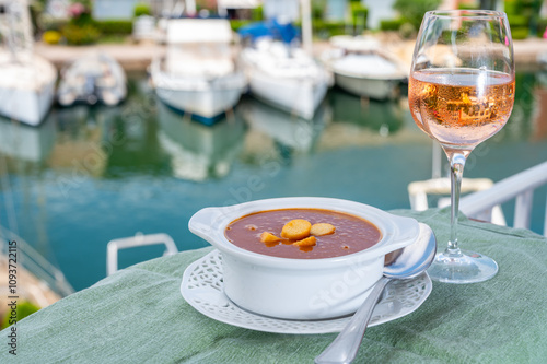 Homemade tasty fish or bisque soup with croutons served with glass of cold rose wine and view on yacht boats and houses of Port Grimaud, French Riviera, France. Food of Provence photo