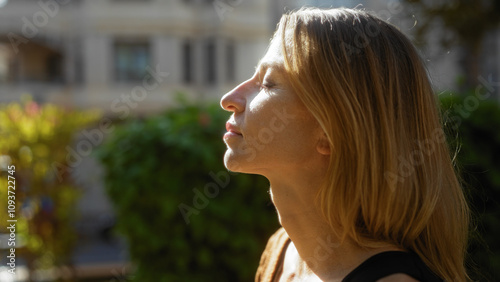 Canvas Print Woman enjoying sunlight with closed eyes in an urban park setting, surrounded by greenery and city architecture, capturing a serene outdoor moment