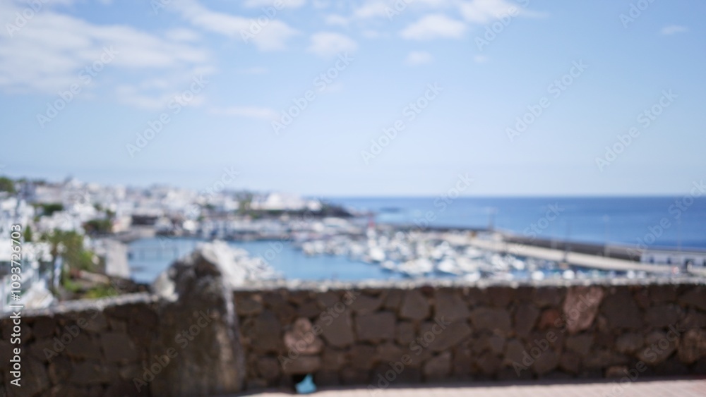 Fototapeta premium Defocused image of the marina in lanzarote, canary islands, showing a blurry background with boats and cityscape under a clear blue sky