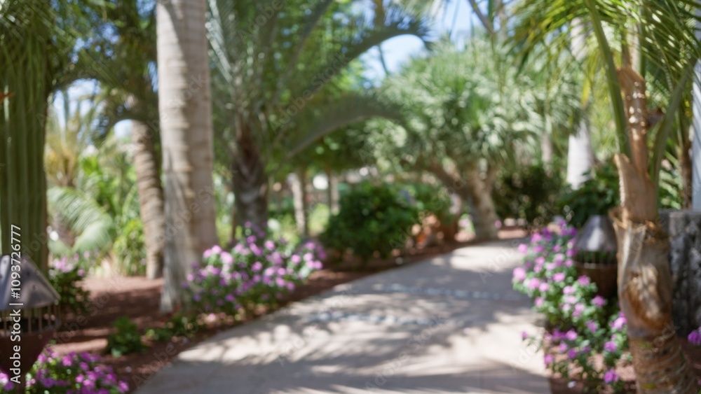 Blurred tropical resort pathway with lush greenery and colorful flowers under bright sunlight