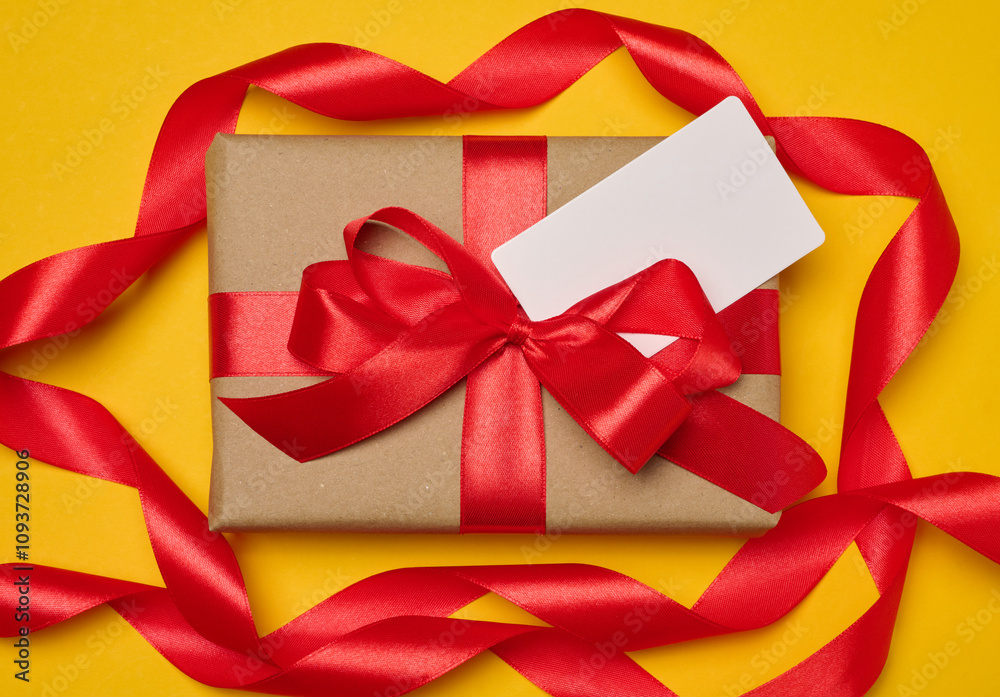 Box tied with red ribbon on yellow background, festive background Box tied with red ribbon on yellow background, festive background