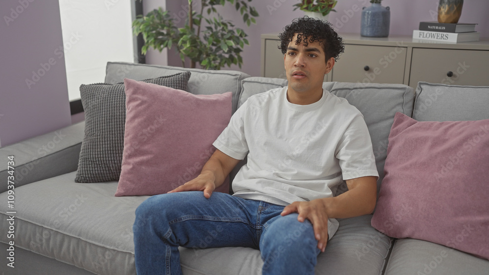 A young hispanic man relaxing on a gray couch in a modern living room interior with decorative pillows and houseplants A young hispanic man relaxing on a gray couch in a modern living room interior with decorative pillows and houseplants