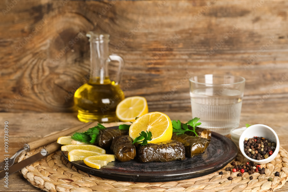 Plate with tasty Dolmas (stuffed grape leaves), lemon, spices and oil on wooden background