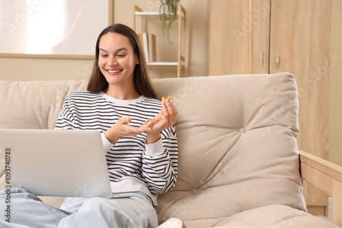 Young woman with laptop and ear plugs sitting on sofa at home