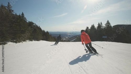 4K video of a couple man and woman skiers alpine skiing on cold winter snow at a ski resort mountain with sunshine. Adventure and thrill while on vacation and holiday. Killington, Vermont, USA.