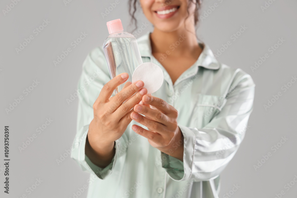 Young African-American woman with bottle of micellar water and cotton pad on grey background, closeup Young African-American woman with bottle of micellar water and cotton pad on grey background, closeup