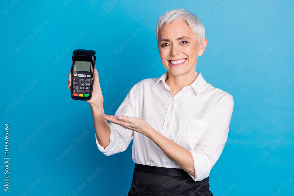 Photo of lovely pensioner lady point hold terminal serve clients coffee shop dressed waitress uniform isolated on blue color background Photo of lovely pensioner lady point hold terminal serve clients coffee shop dressed waitress uniform isolated on blue color background