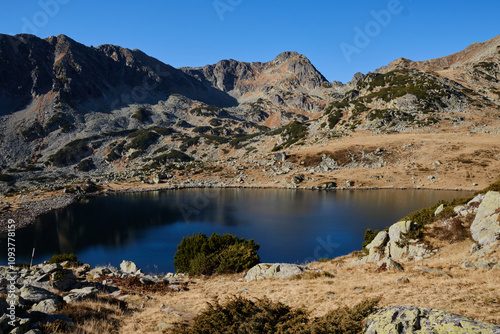 Serene mountain lake nestled in a picturesque valley. Crystal-clear waters reflect the rugged peaks under a clear blue sky. Ideal for travel, nature, and landscape projects.