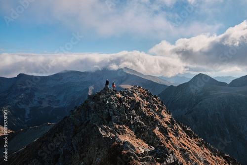 Hikers on a mountain peak enjoy a breathtaking panoramic view of a vast, cloud-covered mountain range.  A stunning landscape photo perfect for adventure, travel, and nature themes. photo