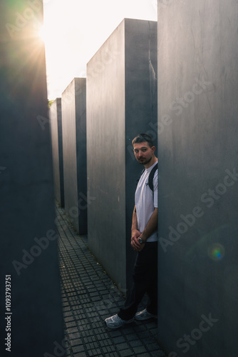 A man wearing a white shirt leans casually against a nearby wall