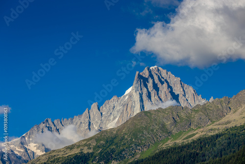 Petit Dru granite mountain wall and summit in Chamonix valley, french Alps. Prominent mountain peak in the Alps, stunning landscape view of the rocky peak covered with clouds, snow and ice