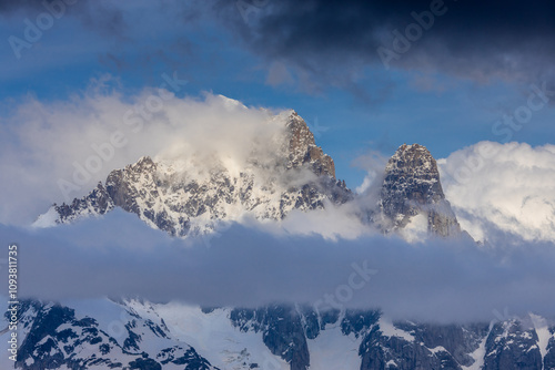 Petit Dru granite mountain wall and summit in Chamonix valley, french Alps. Prominent mountain peak in the Alps, stunning landscape view of the rocky peak covered with clouds, snow and ice