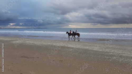 Riding horses on the shoreline beneath a cloudy sky in the early morning