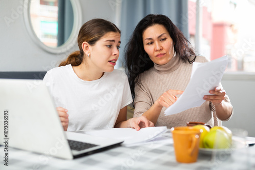 Two women with financial documents near laptop sitting at the table at home