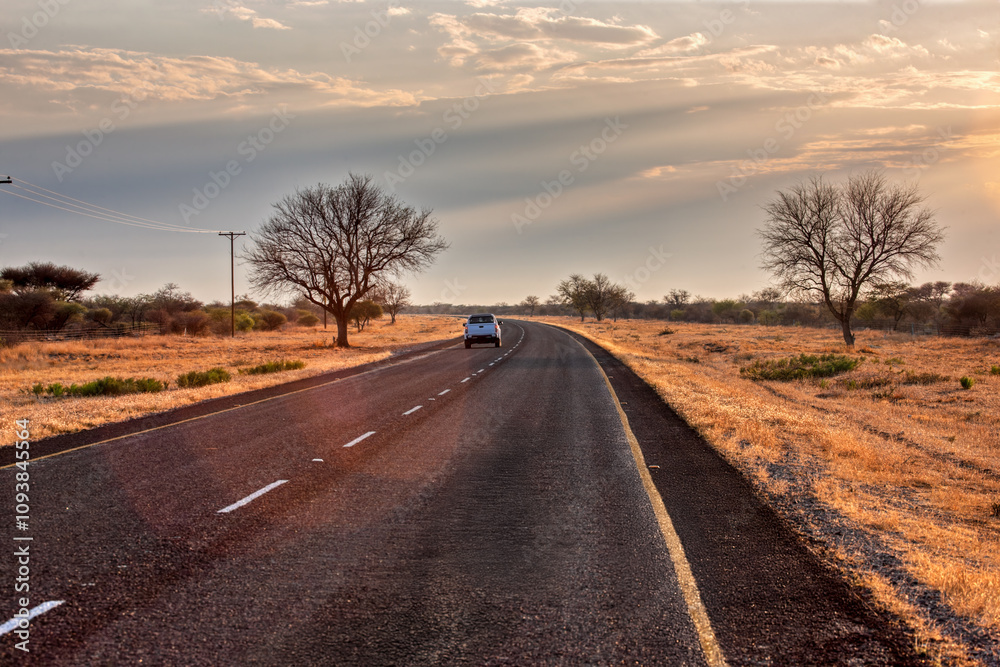 Fototapeta premium african road highway at sunset perspective, car far away dry land outback