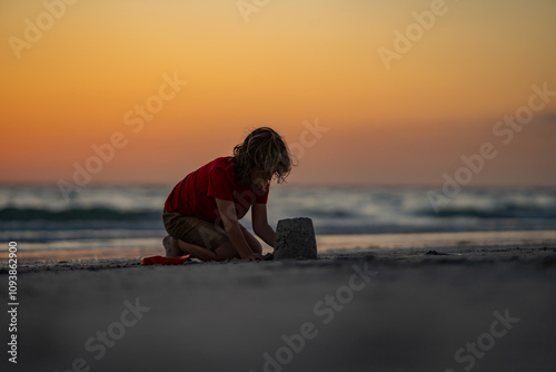 Kid building sandcastle. Kid playing on the beach. Child playing in the sand on tropical beach on sunset. Sand castle for summer kids. Kid on the sea.