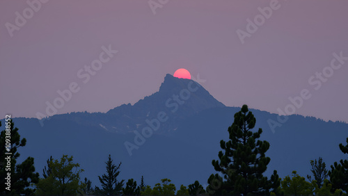 mountains dominating backdrop, trees populating the foreground, a red sun atop the peak