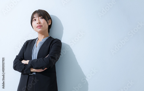 Challenging, sassy looking young woman in a suit looking up at you with her arms crossed in a business setting.