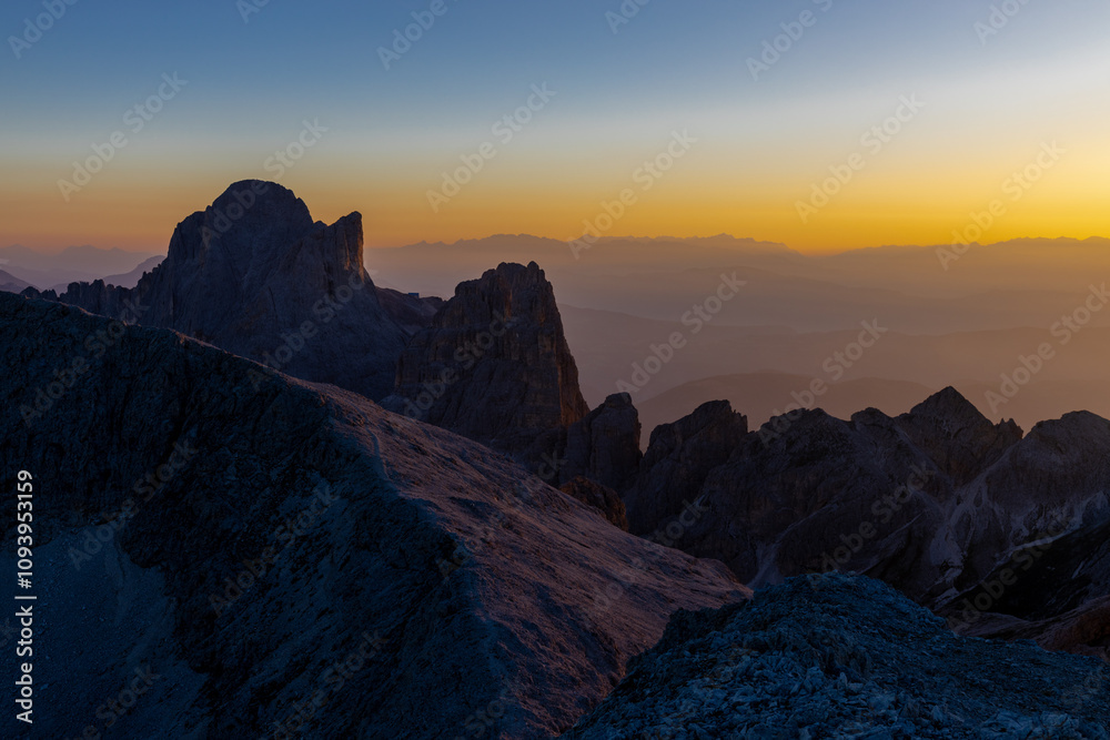 Sunset in the mountains. Red and orange burning sky horizon behind the alpine mountain range. Rocky mountain peaks of the Dolomites at sunset and dawn at sunrise light sunrays going through the clouds Sunset in the mountains. Red and orange burning sky horizon behind the alpine mountain range. Rocky mountain peaks of the Dolomites at sunset and dawn at sunrise light sunrays going through the clouds