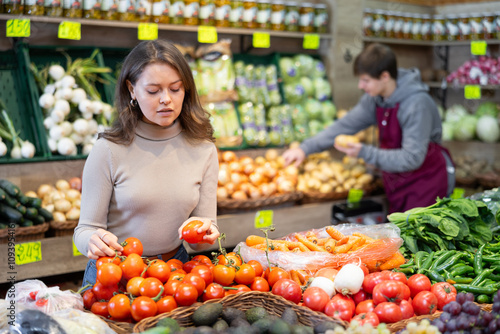 Pleased young female buyer purchasing tomatoes in grocery store with large assortment