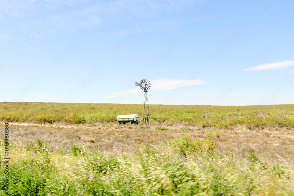 Windmill in a field on the side of the road, in La Pampa, Argentina. Peaceful scene showing renewable energy generation in rural areas. Windmill in a field on the side of the road, in La Pampa, Argentina. Peaceful scene showing renewable energy generation in rural areas.