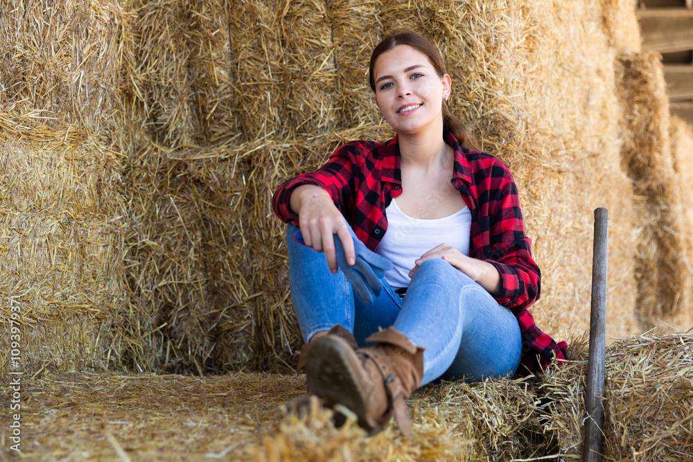 Portrait of a young positive farmer girl resting on haystacks during a work break. Close-up portrait Portrait of a young positive farmer girl resting on haystacks during a work break. Close-up portrait