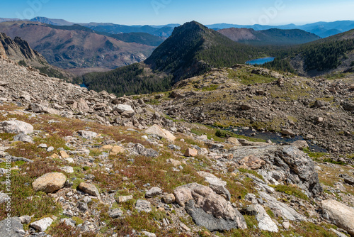 Stunning mountain landscape showcasing rocky terrain, lush greenery, and distant hills under a clear blue sky in the early afternoon