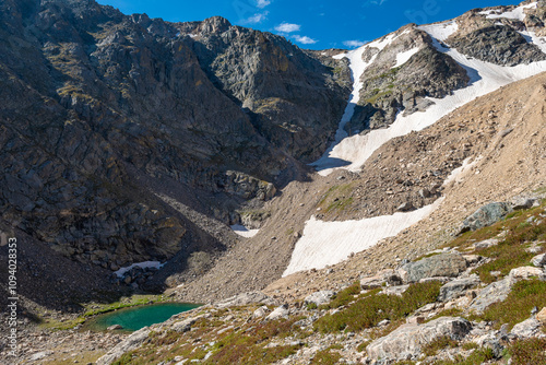 A serene mountain landscape featuring a glacial lake surrounded by rocky cliffs and patches of snow during a clear sunny day. Ptarmigan lake. photo