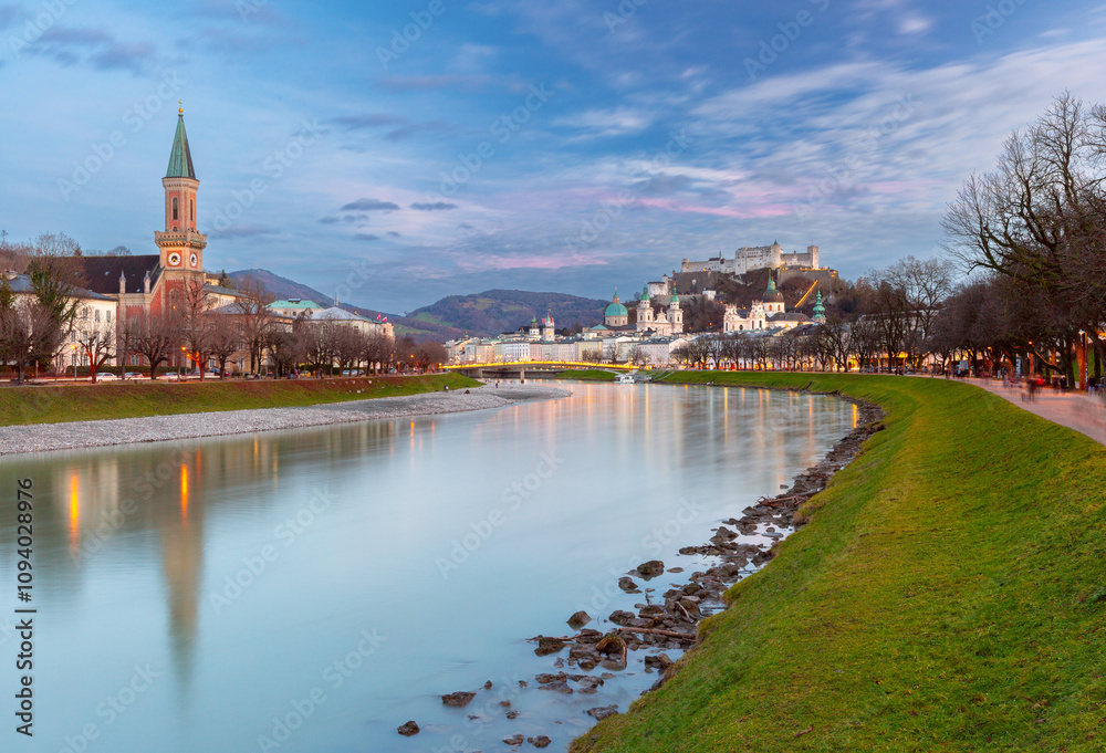 Obraz premium A serene view of the Salzach River in Salzburg, Austria, with reflections of St. Andrew's Church and the Hohensalzburg Fortress in the water