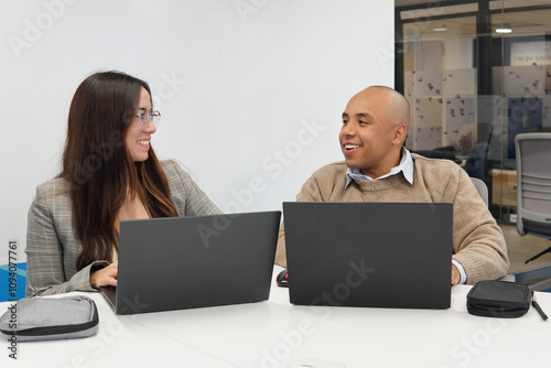 Two people are sitting at a table with two laptops in front of them