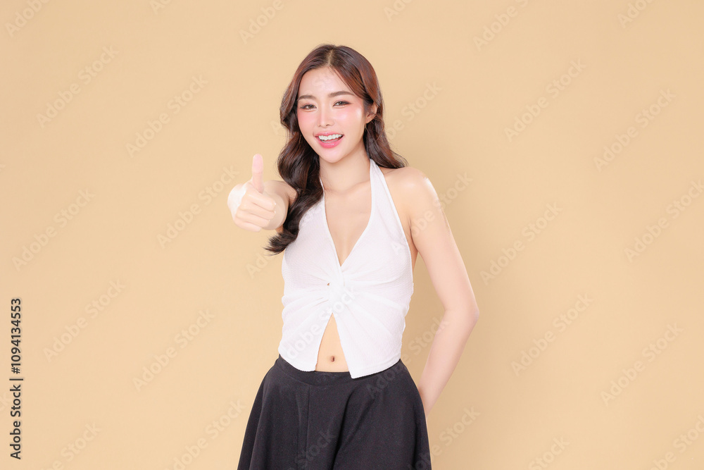 Pretty Asian beauty woman curly long hair with Korean makeup glowing face and healthy facial skin portrait smile showing trump up on isolated beige background. Pretty Asian beauty woman curly long hair with Korean makeup glowing face and healthy facial skin portrait smile showing trump up on isolated beige background.