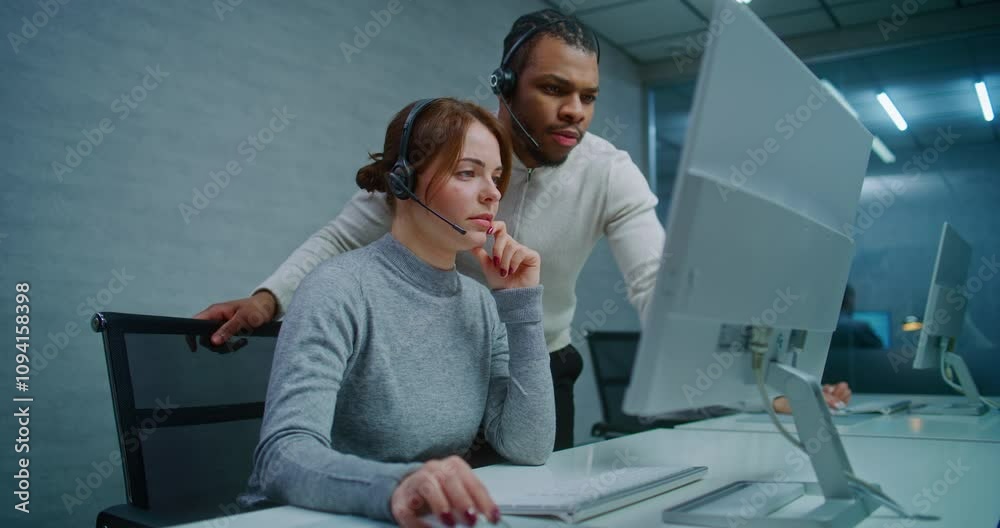 Modern call center office: Two multiethnic hotline operators in headsets talk and discuss work monitoring data on computer. Team of technical support specialists working in online customer support. Modern call center office: Two multiethnic hotline operators in headsets talk and discuss work monitoring data on computer. Team of technical support specialists working in online customer support.