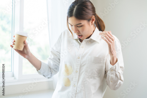 Cloth stain, disappointment asian young woman clumsy with hot coffee, tea stains on shirt, hand show making spill drop on white t-shirt, spot dirty or smudge on clothes at home, isolated on background