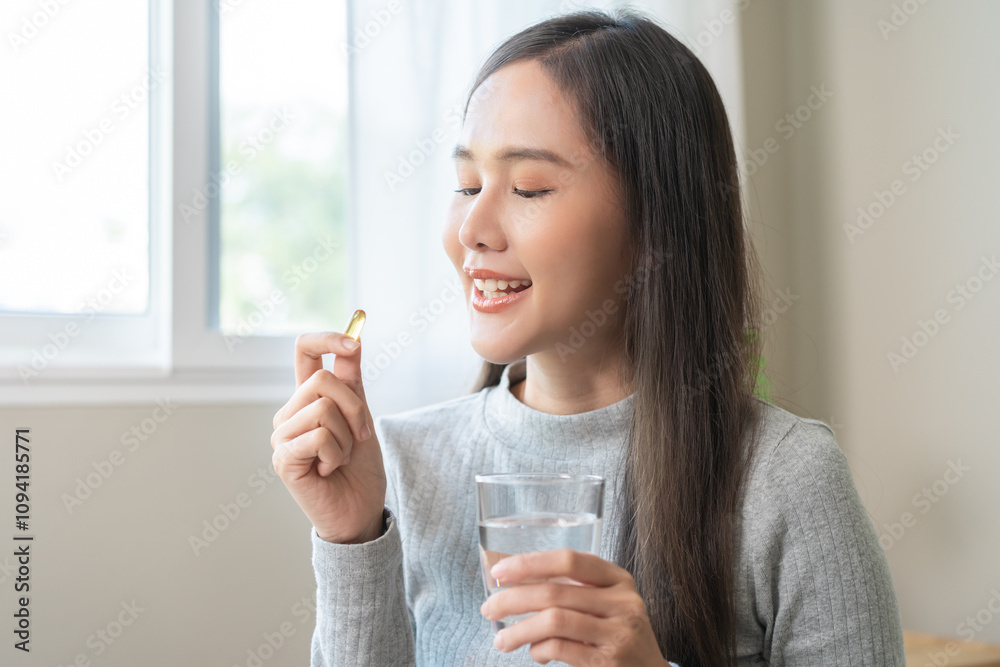 Dietary supplement, asian young woman, girl hand holding fish oil pills, drugs medical, take or eat vitamin for treatment skin, hair and nail strengthen with glass of water at home. Healthcare concept Dietary supplement, asian young woman, girl hand holding fish oil pills, drugs medical, take or eat vitamin for treatment skin, hair and nail strengthen with glass of water at home. Healthcare concept