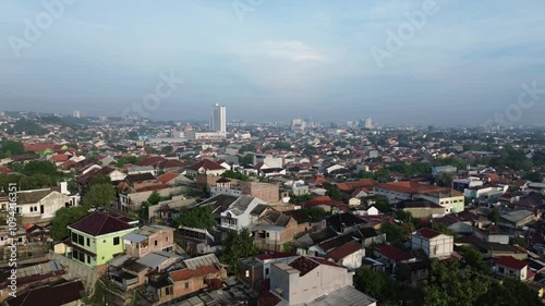 Aerial footage revealing Semarang's cityscape with iconic white tower in the distance, morning light illuminating mix of modern and traditional architecture photo