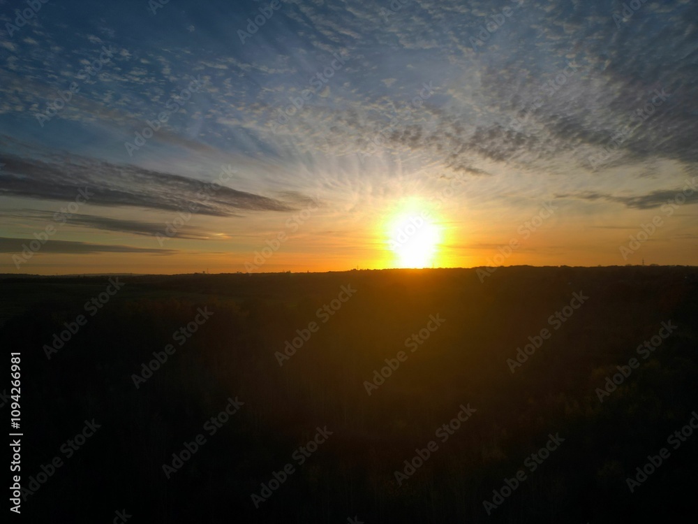 Naklejka premium Stunning sunset over a vast landscape with dramatic clouds and a glowing horizon.