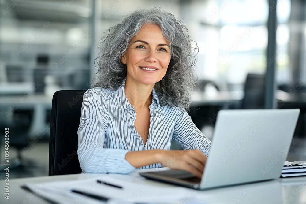 Middle-aged woman smiling working on laptop in modern office at desk professional business environment Middle-aged woman smiling working on laptop in modern office at desk professional business environment