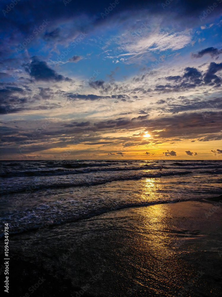 Obraz premium Colorful beach sunset with deep sky and clouds, sun rails over the sea waves